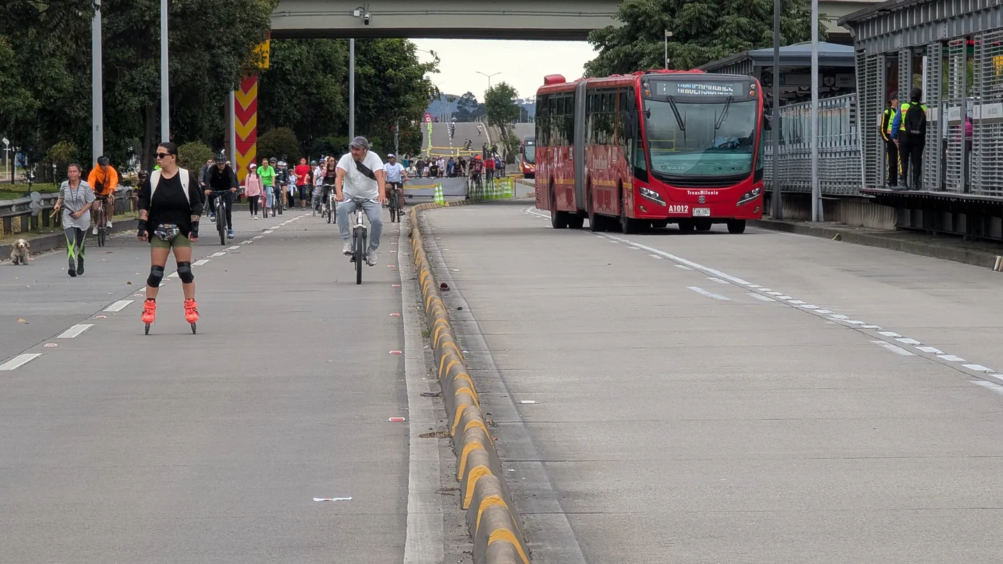 Una patinadora y un ciclista circulan por la calzada cerrada de la Ciclovía, junto a un bus de TransMilenio detenido